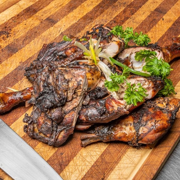 Grilled jerk chicken pieces, garnished with parsley and scallions, on a striped wooden cutting board.