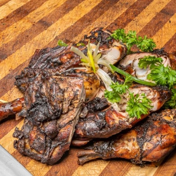Grilled jerk chicken pieces, garnished with fresh parsley and sliced scallions on a wooden board.