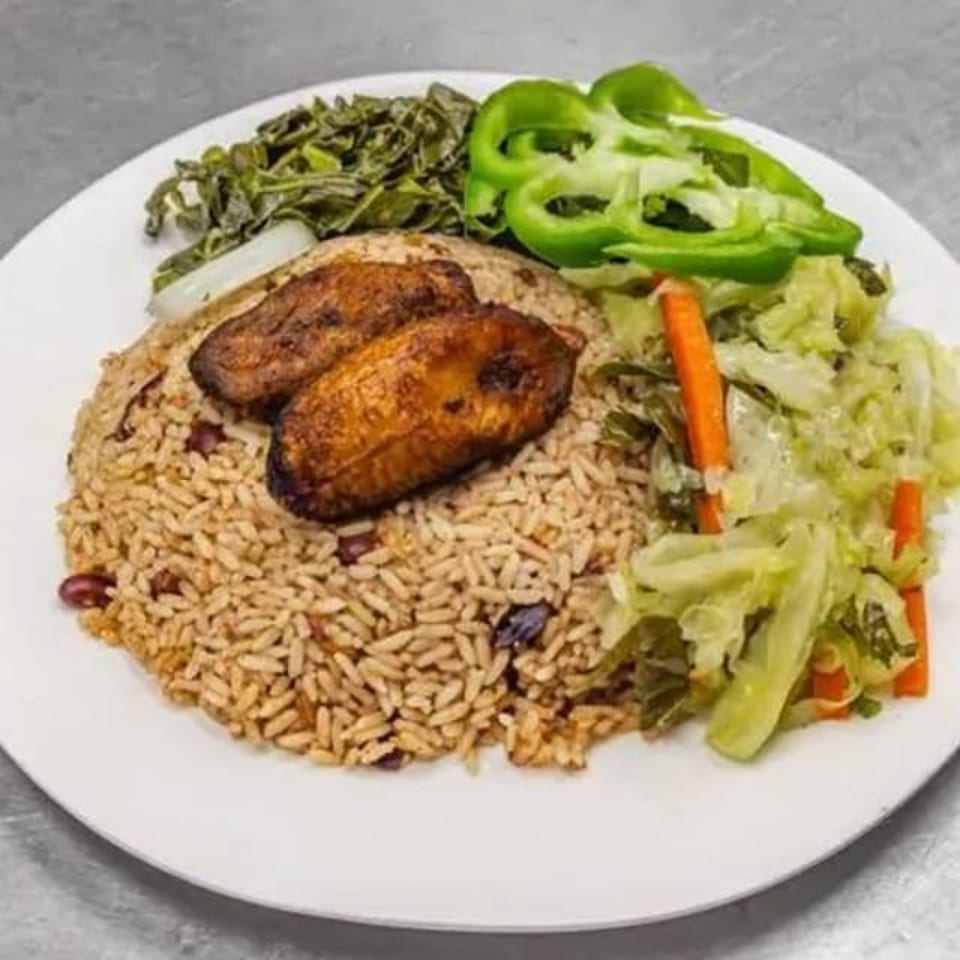 A plate of rice and peas with two fried plantains, steamed cabbage, and green peppers.