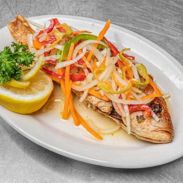 Whole fried fish topped with colorful pickled vegetables, garnished with lemon and parsley.