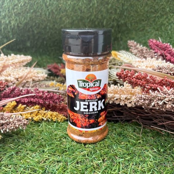 Tropical Spices Jamaican Jerk Seasoning bottle on green grass with dried floral arrangements.