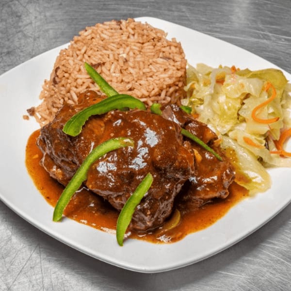 Braised oxtail with rice and peas, topped with green peppers, and a side of steamed cabbage.