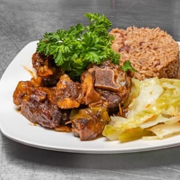 A plate of oxtail stew with rice and peas, garnished with parsley, and a side of steamed cabbage.